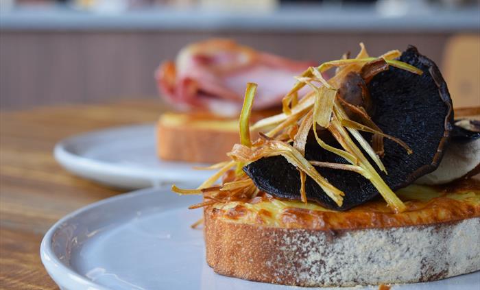 A close up picture of a Welsh Rarebit meal, topped with crispy onions and large mushrooms on white crusty bread.